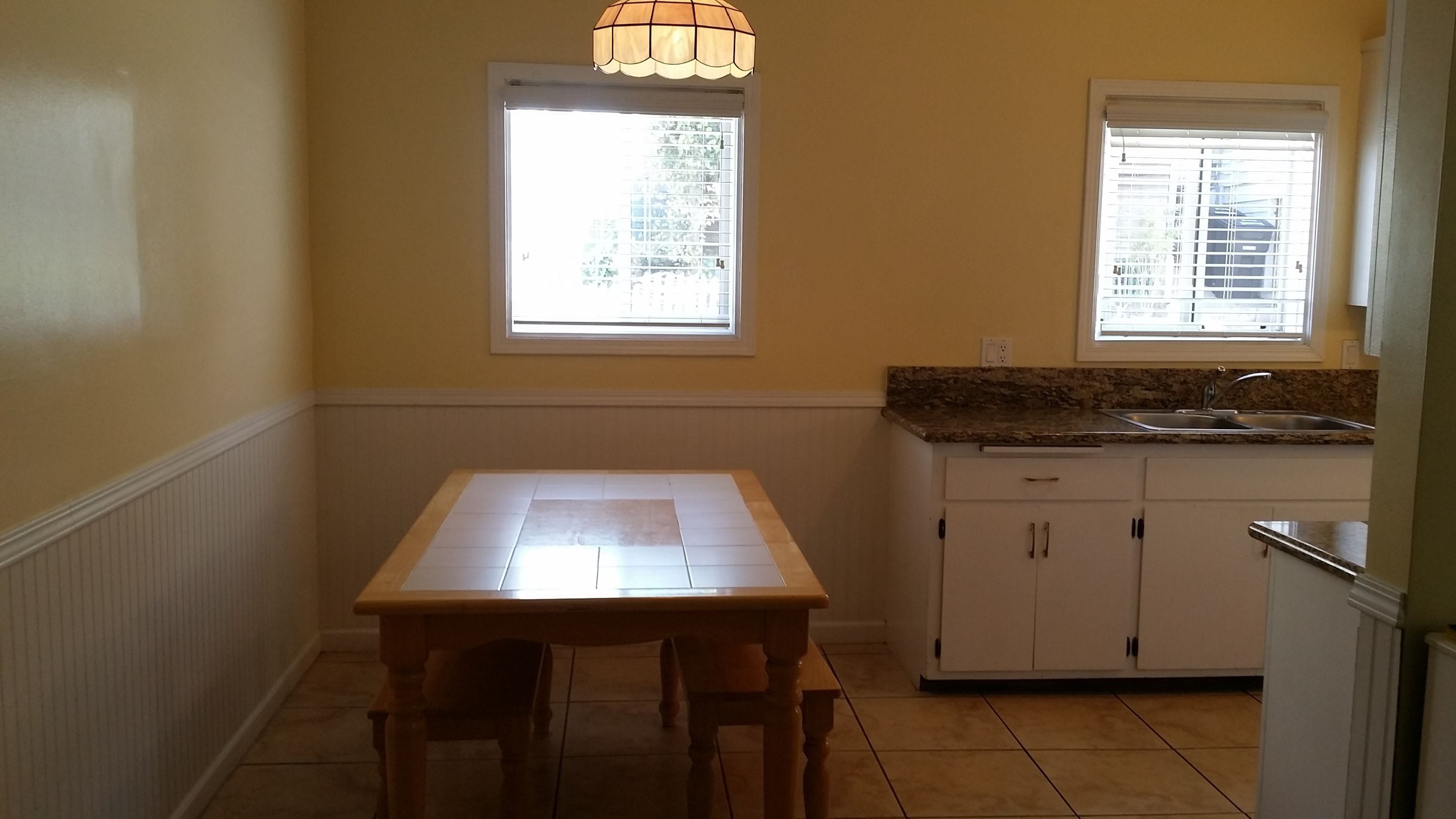 A small kitchen with a dining table, two windows, and a sink.