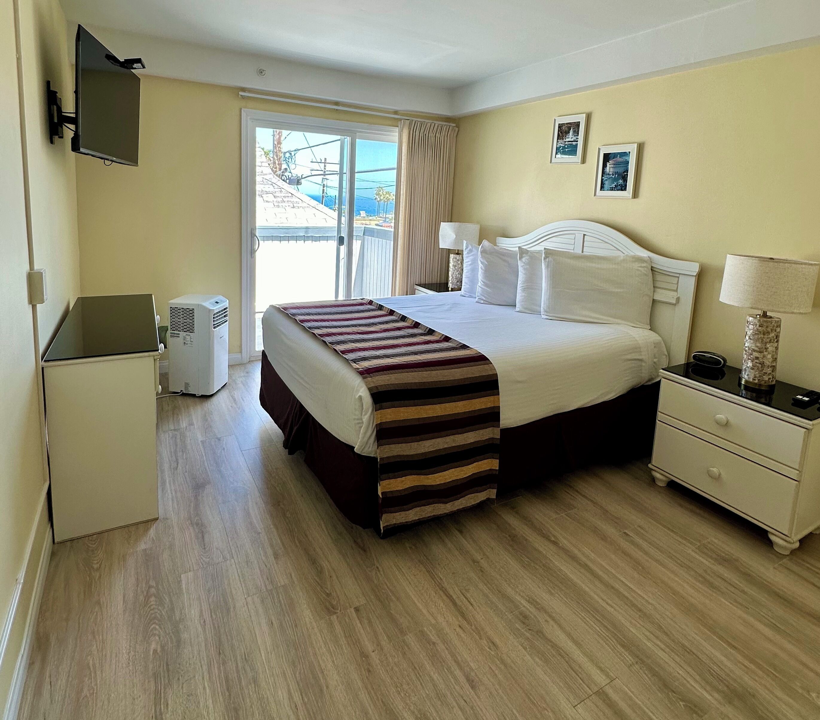 A hotel room with a bed, bedside tables, a TV mounted on the wall, and a window with a view of the outside.