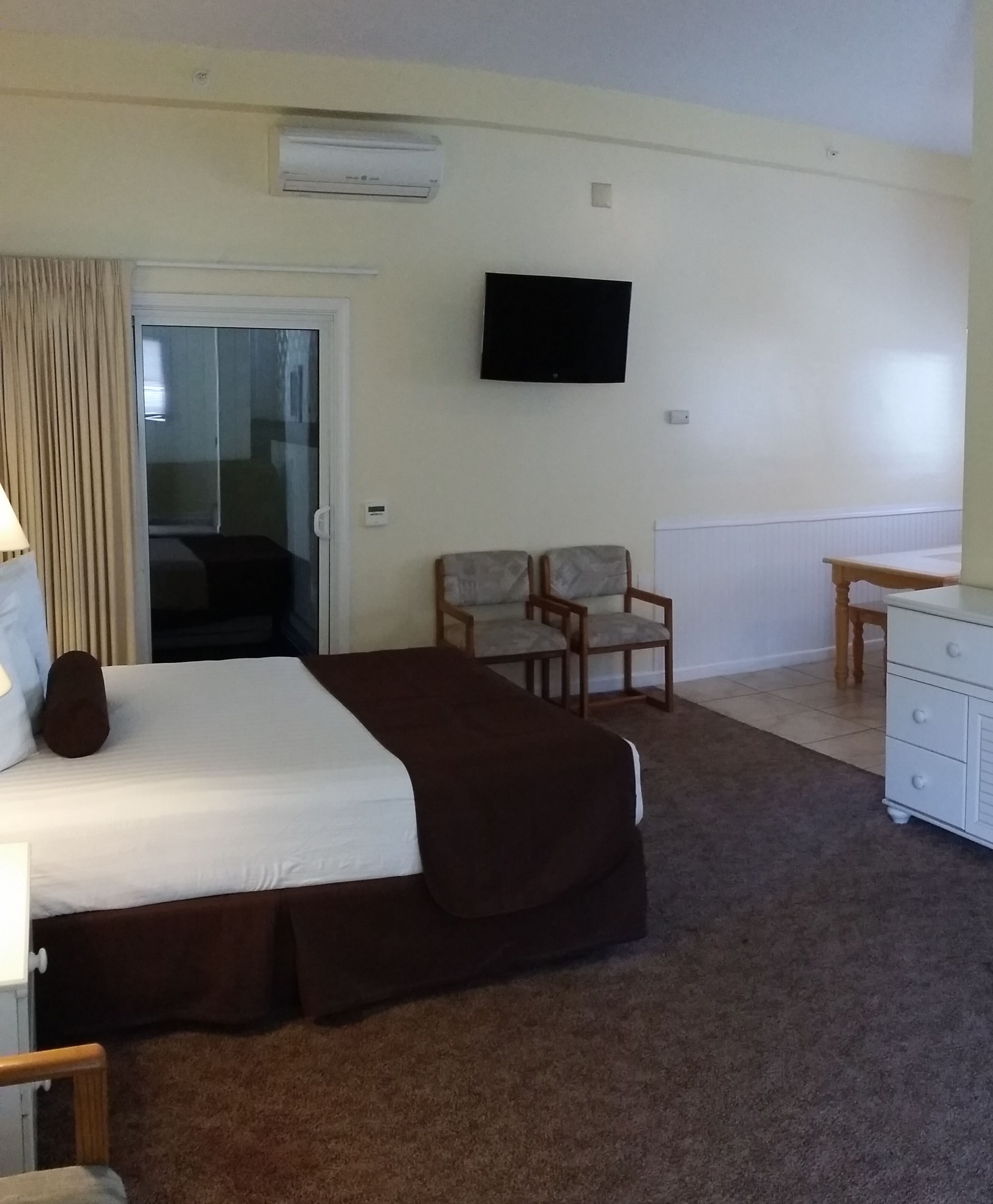 A hotel room with a bed, a desk, two chairs, a television, and an air conditioning unit.