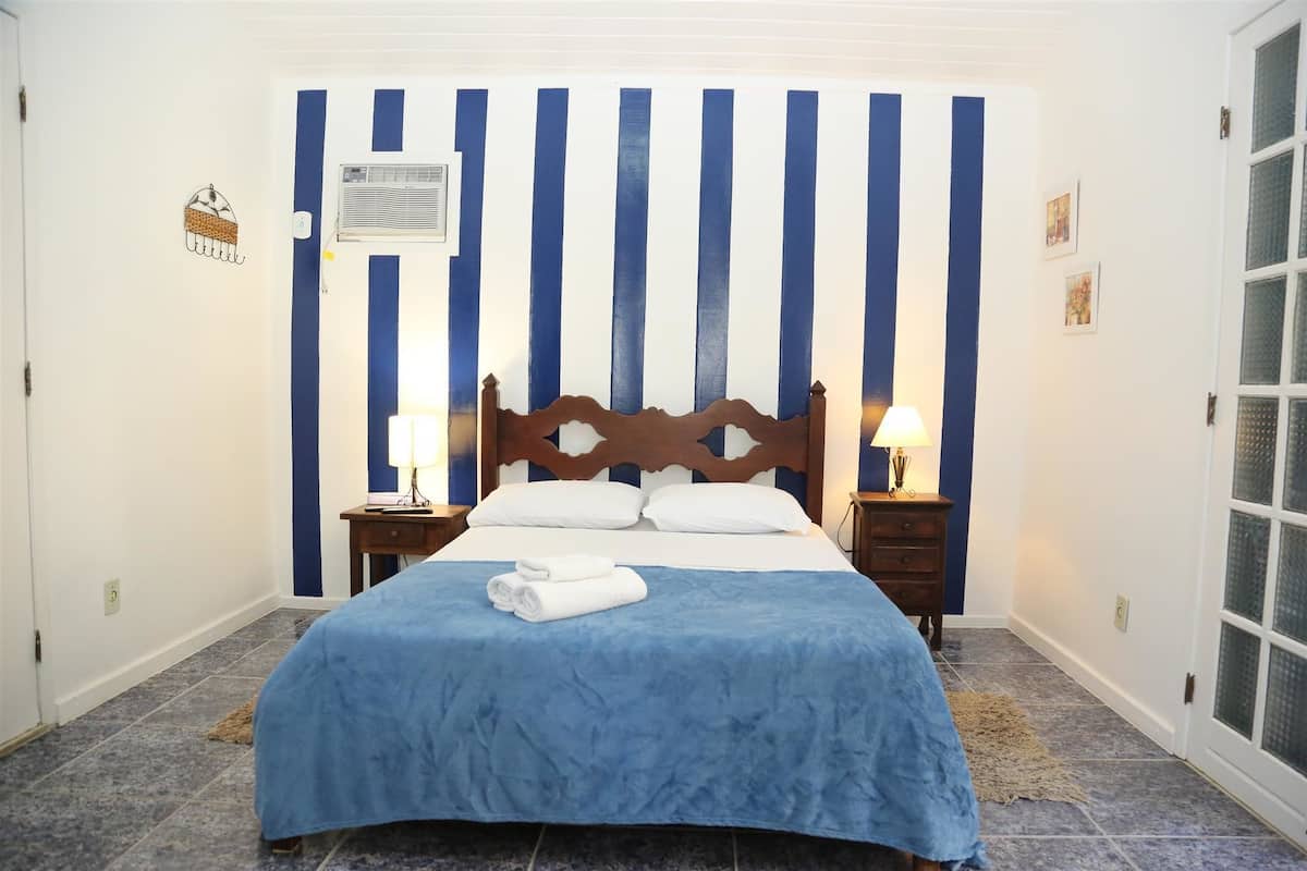 Ein Schlafzimmer mit einem Bett, zwei Nachttischen, einem Fenster und einer Wand mit vertikalen blauen und weißen Streifen.