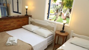 Un dormitorio con cama, una mesita de madera, una lámpara y ventana con vista al jardín.