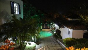 Vista nocturna de un patio con un camino empedrado que lleva a una entrada portonada.
