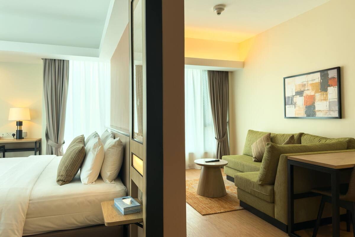 Een hotelkamer met een bed, een bureau, een groene bank en een schilderij aan de muur.