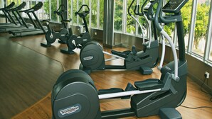 Une salle de sport équipée de plusieurs tapis de course et de plusieurs appareils elliptiques, de grandes fenêtres offrant une vue sur la verdure et d’un plancher en bois.