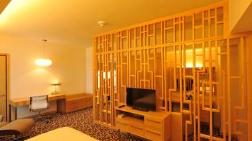 A hotel room with a bed, a TV, a desk with a lamp, and a patterned carpet.