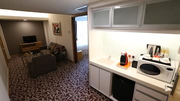 A compact hotel room with a kitchenette, a sofa, a dining area, and a patterned carpet.