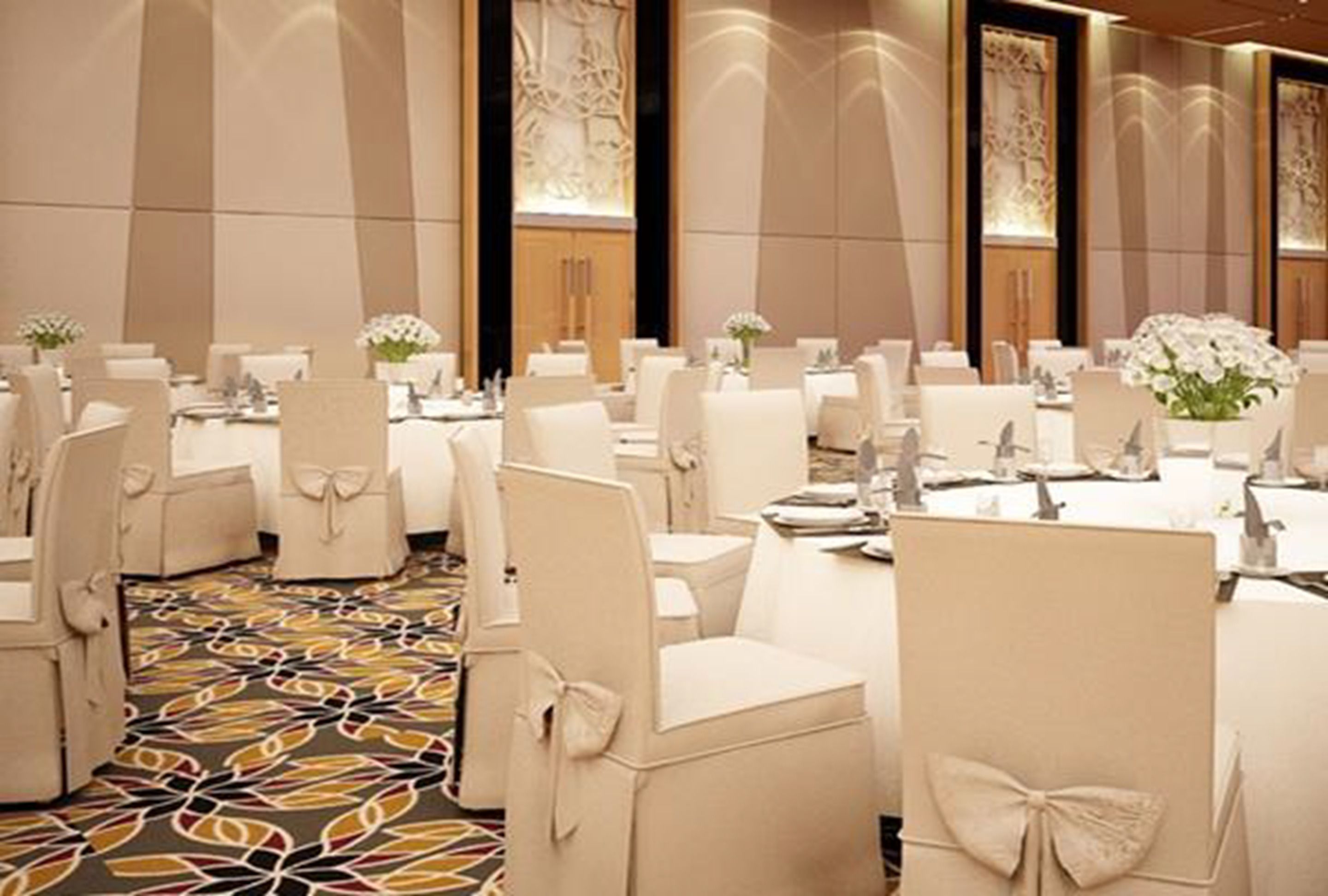 Une salle de banquet avec des tables rondes, des chaises blanches et des centres de table floraux.