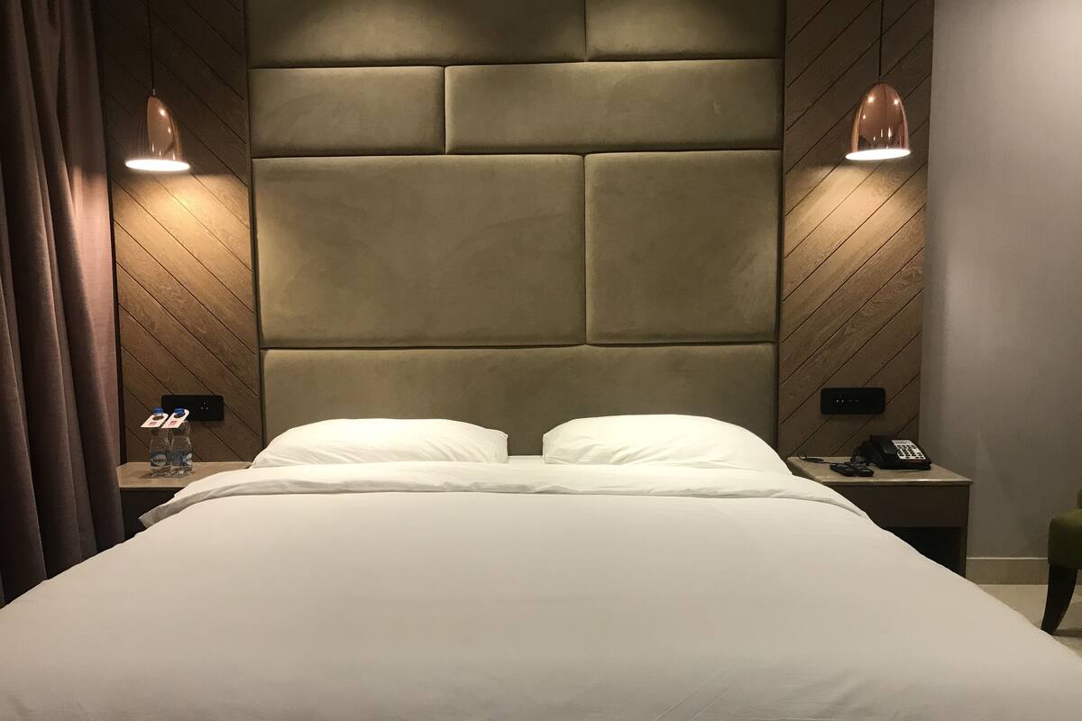 A neatly made bed with a padded headboard, two bedside tables with lamps, and a bottle of water on one table.