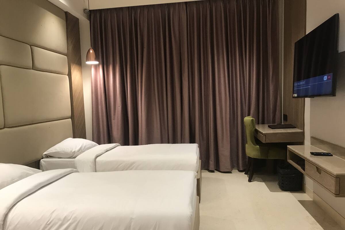 A hotel room with two beds, a desk with a chair, a television, and a large window with curtains.