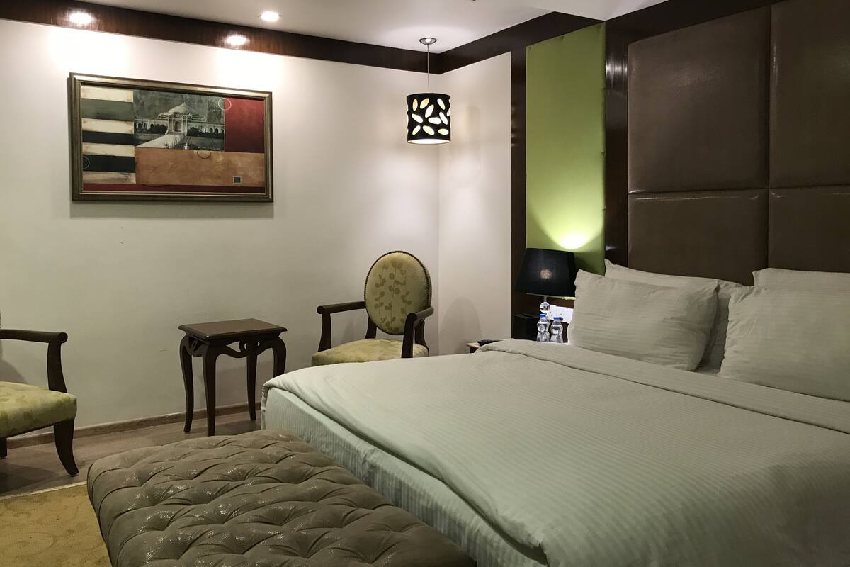 A hotel room with a large bed, a small table, two chairs, a decorative wall piece, and a nightstand with a lamp.