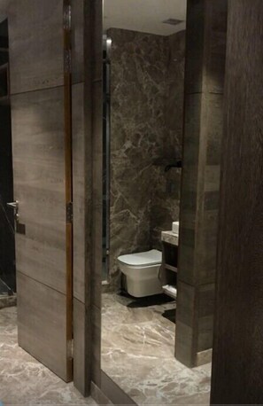 A bathroom with a marble floor, a toilet, and a shower area. - Levana Hotel (Lucknow)