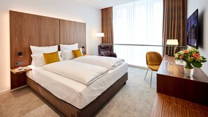 A hotel room with a large bed, a desk with a chair, a TV, and a window with curtains. - Kasino Hotel (Leverkusen)