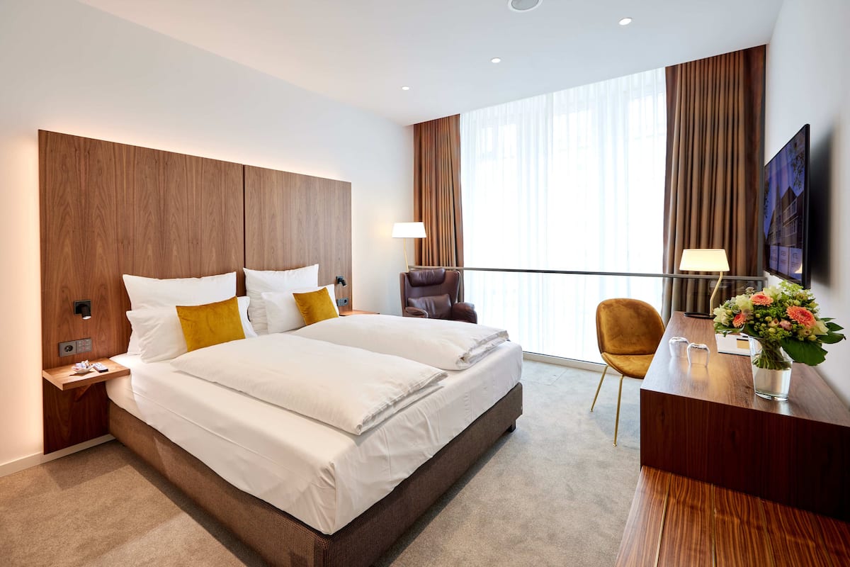 A hotel room with a large bed, a desk with a chair, a TV, and a window with curtains.