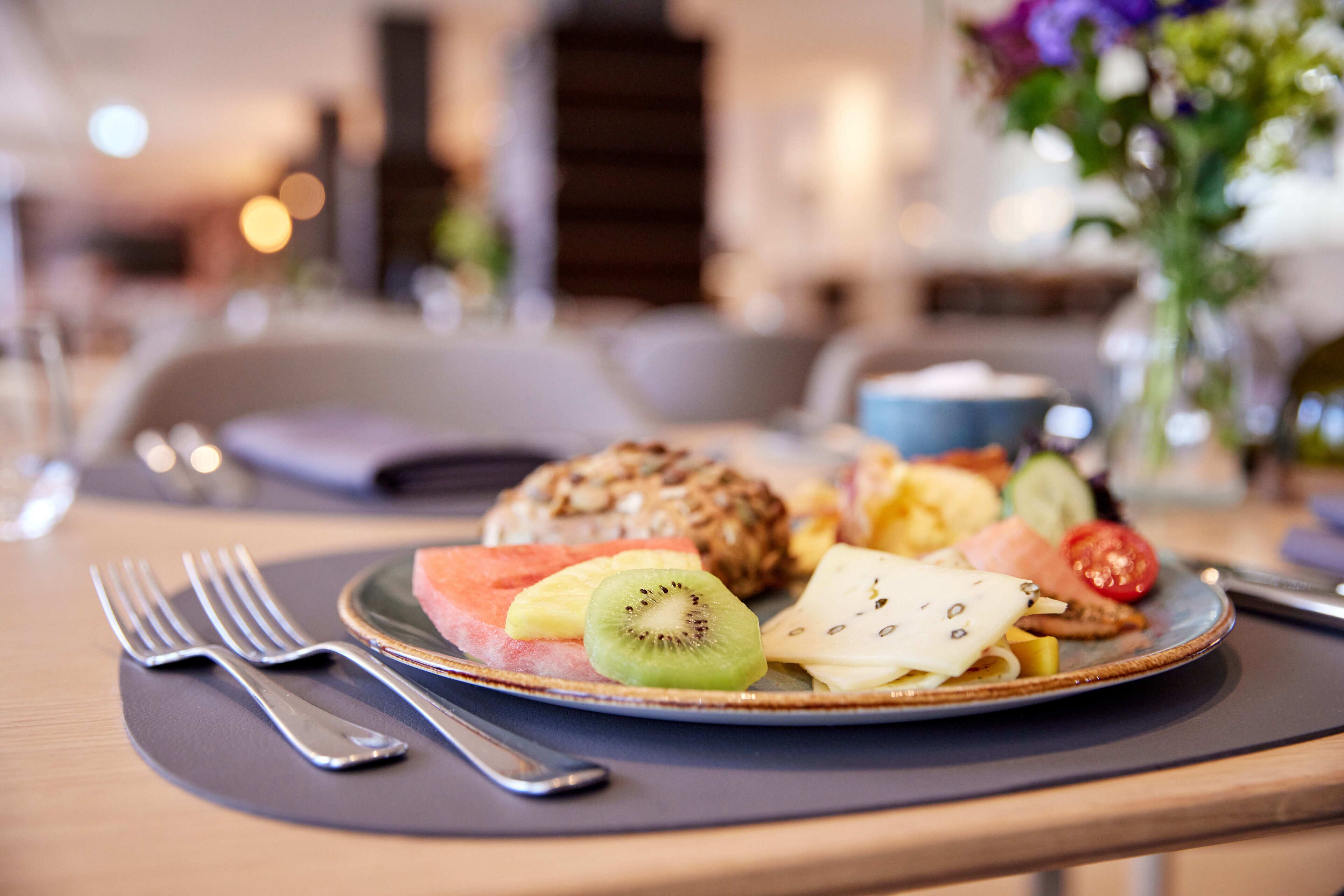 A breakfast plate with fruits and a croissant on a table with a fork and spoon.