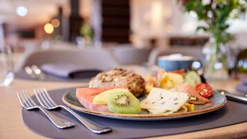 A breakfast plate with fruits and a croissant on a table with a fork and spoon.