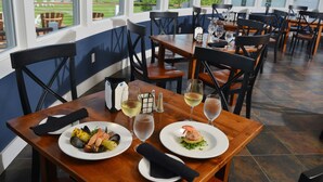 A restaurant with wooden tables and chairs, two plates of seafood, and wine glasses. - Newagen Seaside Inn (Southport)