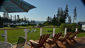 A deck with wooden chairs and a table, overlooking a grassy area with trees and a body of water. - Newagen Seaside Inn (Southport)