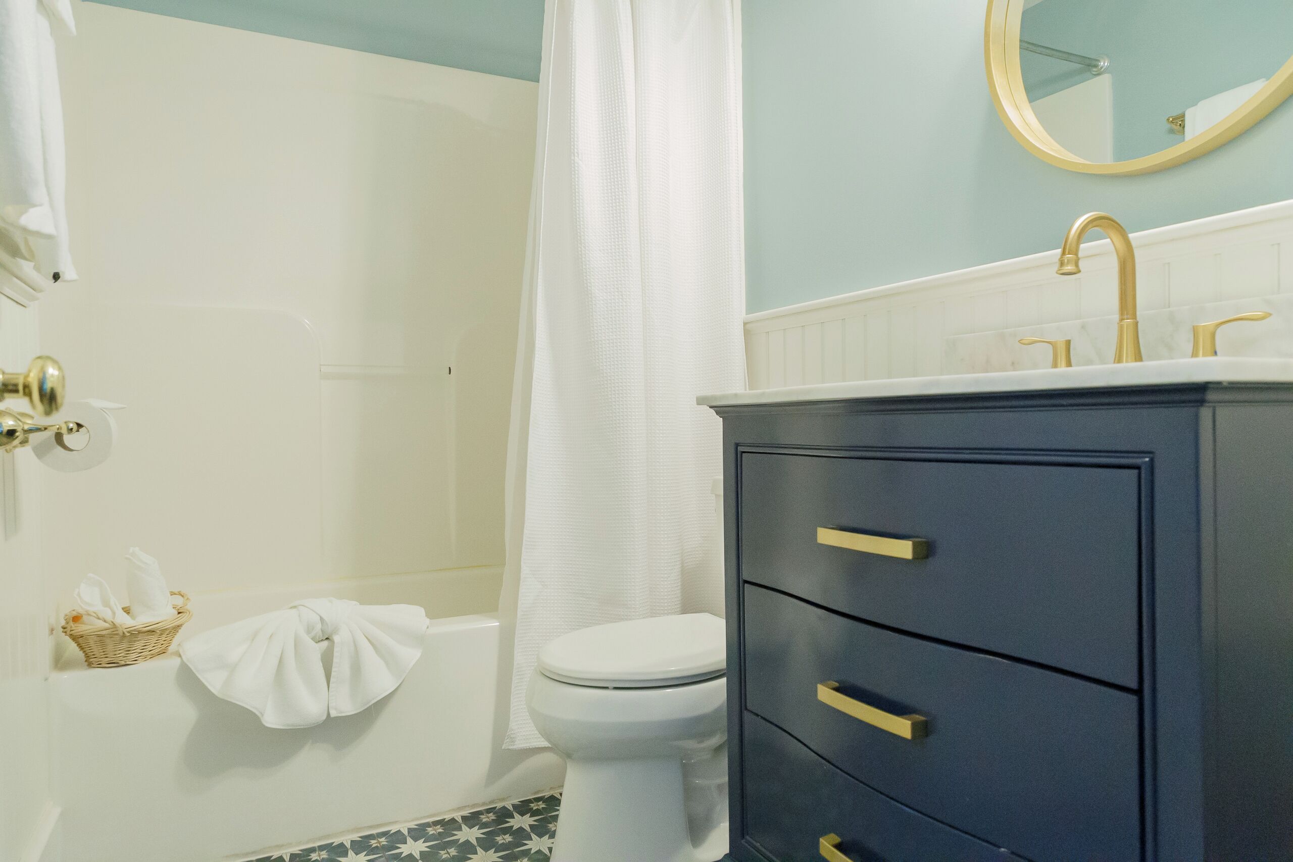 A bathroom with a white toilet, a bathtub, a shower curtain, a vanity with drawers, and a mirror.