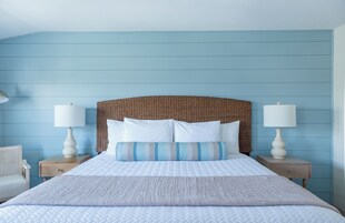 Un dormitorio con una cama grande, dos mesitas de noche, un cabecero de mimbre y una pared azul.