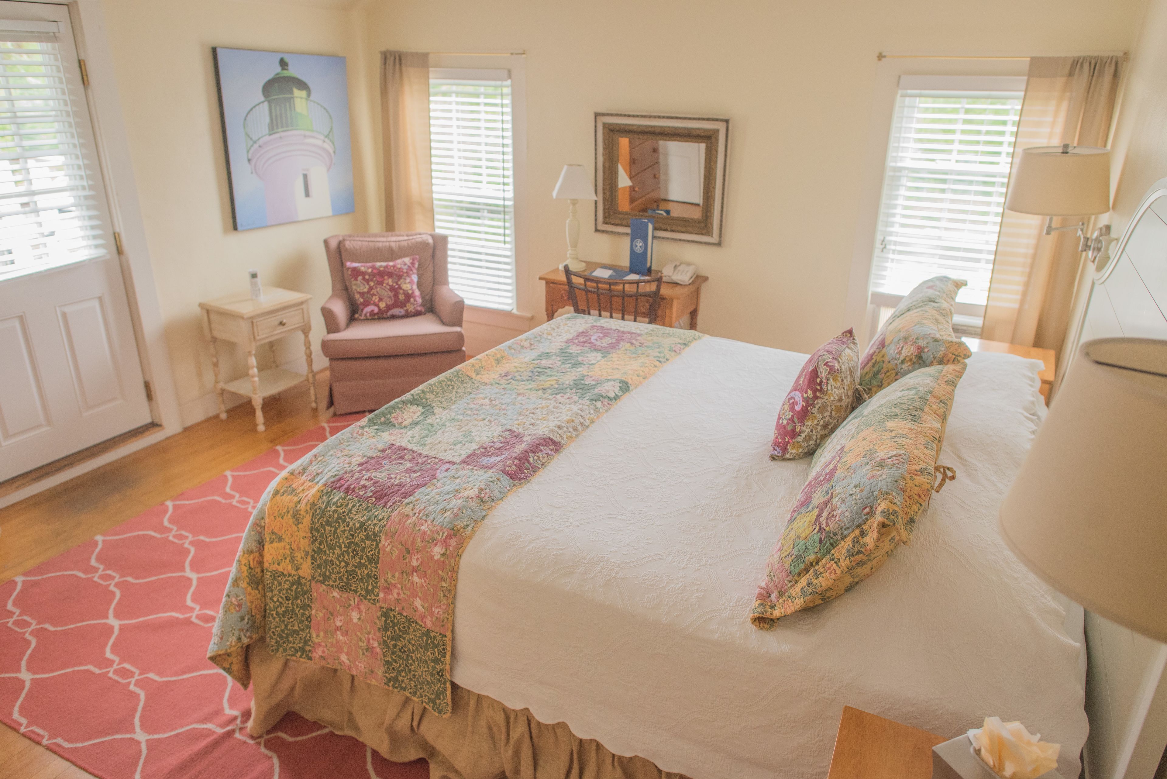A bedroom with a large bed, a chair, a desk, and a painting of a lighthouse.
