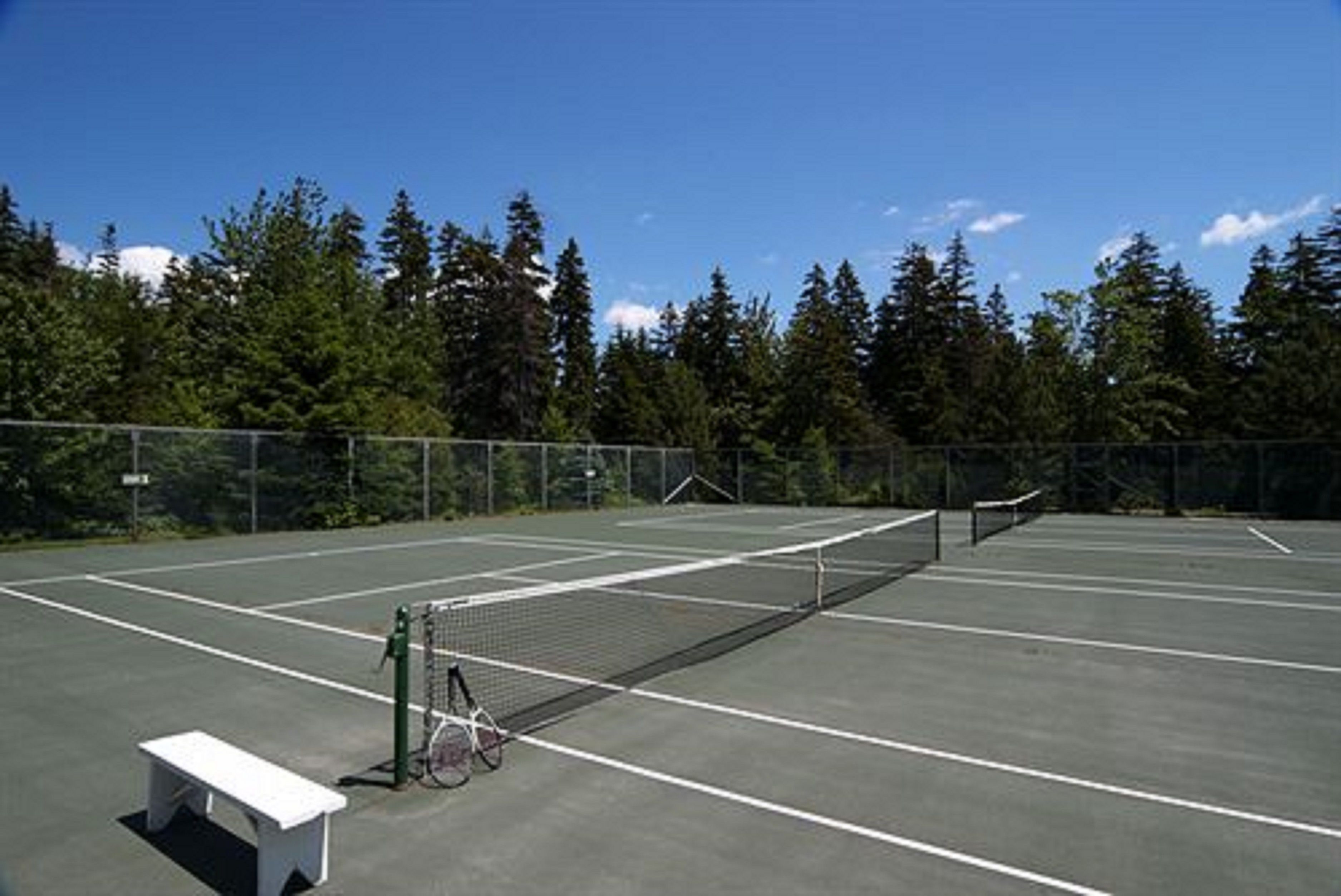 An outdoor tennis court with a bench and a bicycle.