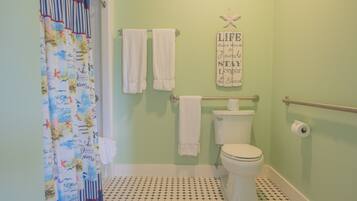 A bathroom with a nautical-themed shower curtain, a toilet, a handrail, and a motivational quote on the wall.