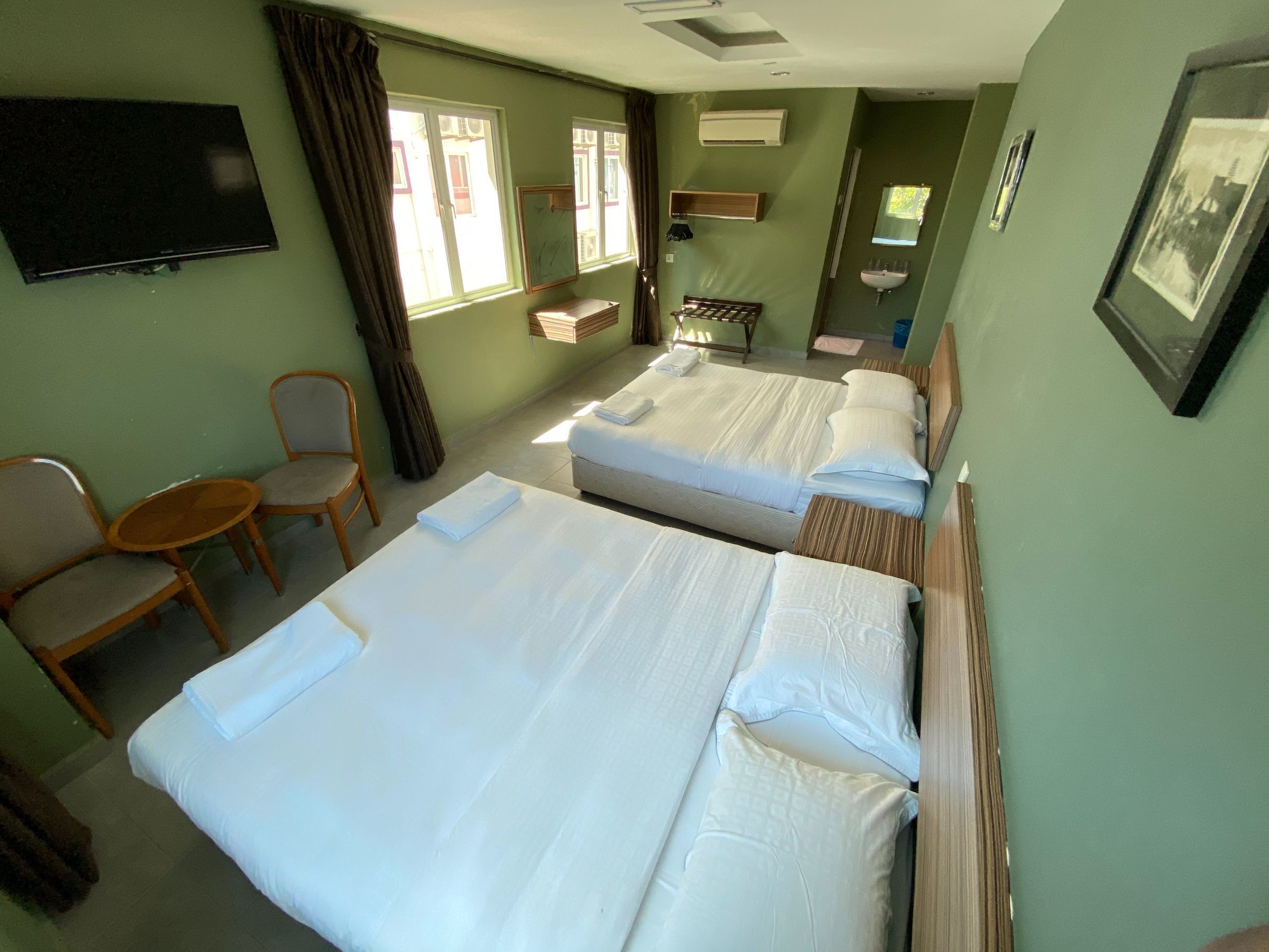 A hotel room with two beds, a TV, a small table, a chair, and a window with curtains.