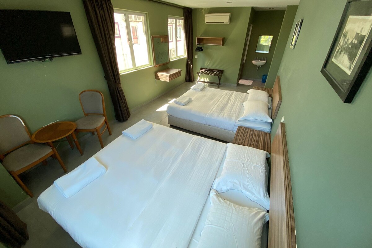 A hotel room with two beds, a TV, a small table, a chair, and a window with curtains.