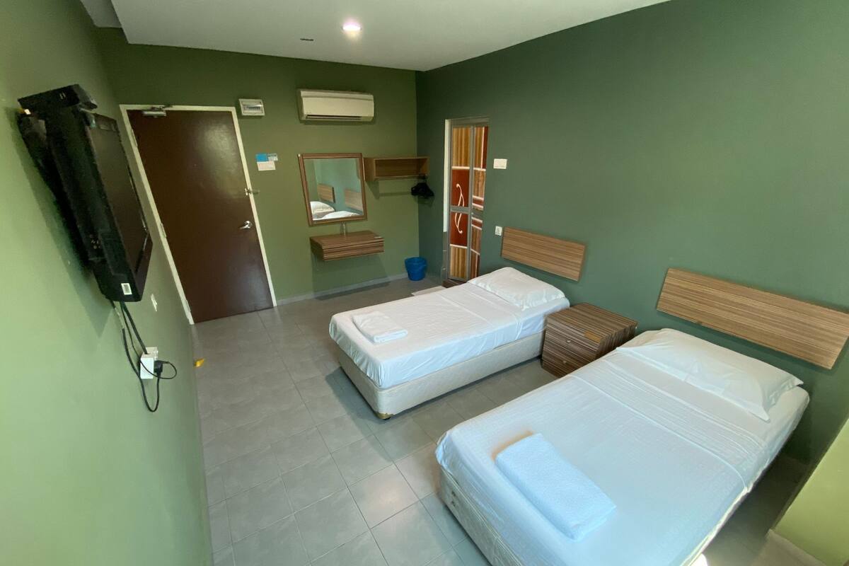 Ein Hotelzimmer mit zwei Einzelbetten, einem Holzkopfteil, einem Spiegel, einem Kleiderschrank und einem Fernseher.