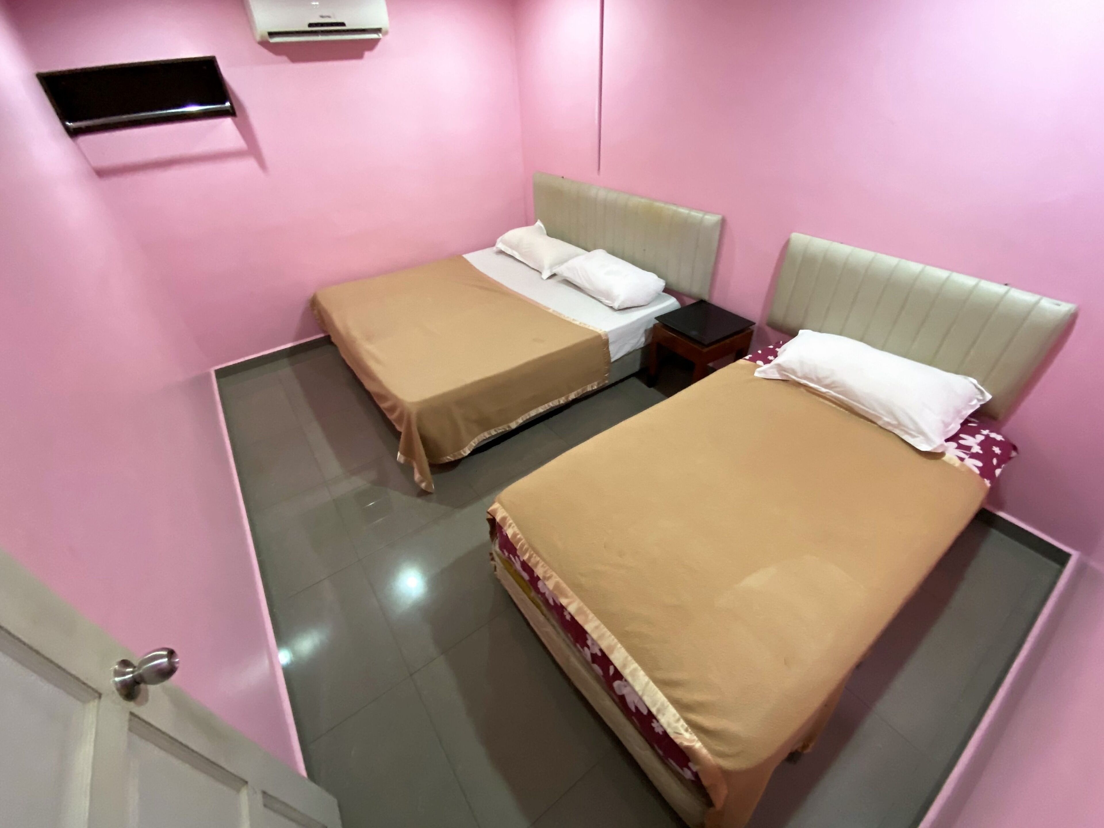 Habitación de hotel con dos camas, una mesita y aire acondicionado instalado en la pared.