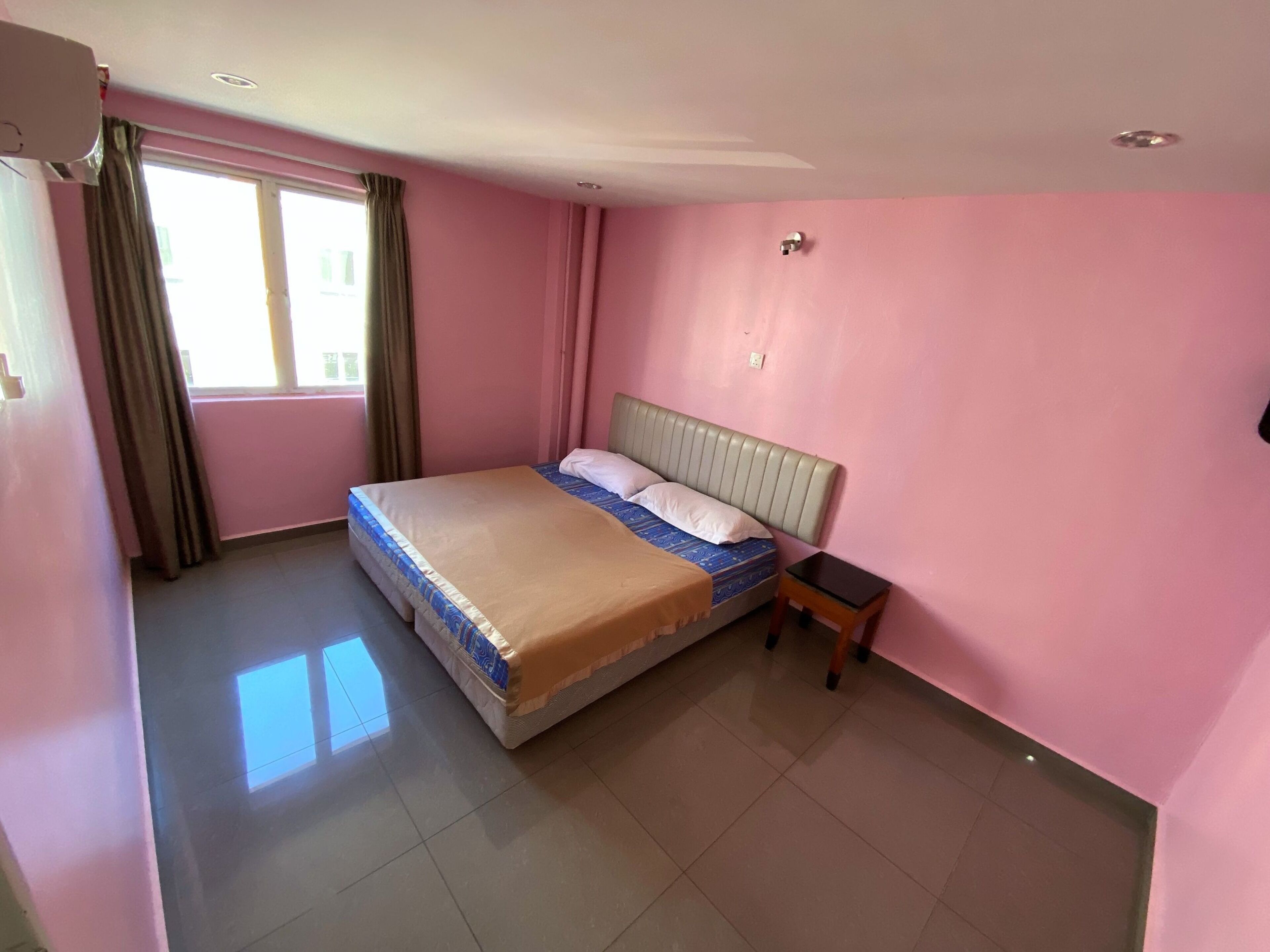 Un dormitorio con cama, mesita de noche, ventana con cortinas y pared rosa.