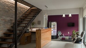 Un intérieur moderne avec un escalier en bois, un comptoir d’accueil, un mur violet et un espace détente comprenant des chaises et une table.