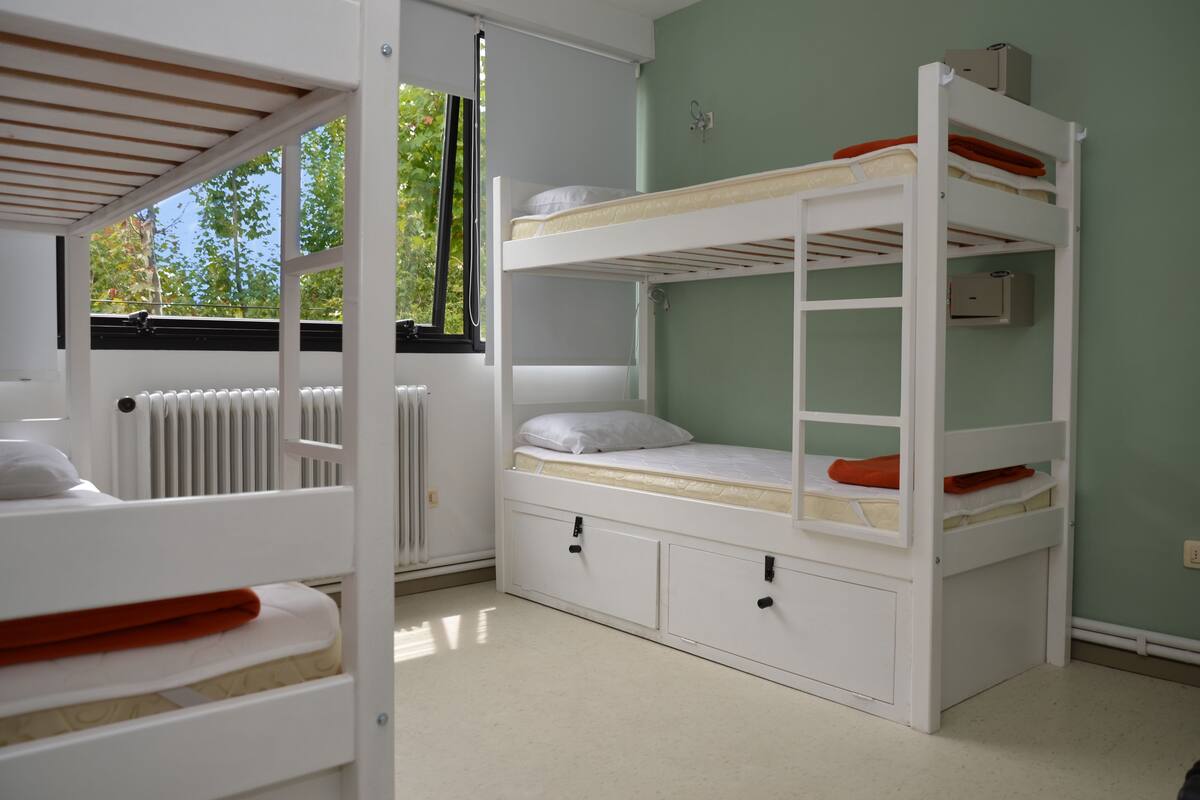 A bunk bed room with a window, a radiator, and a door.