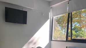 Un lit bien fait, avec une literie blanche, un oreiller noir et une serviette enroulée. Un téléviseur à écran plat est fixé au mur, au-dessus du lit.