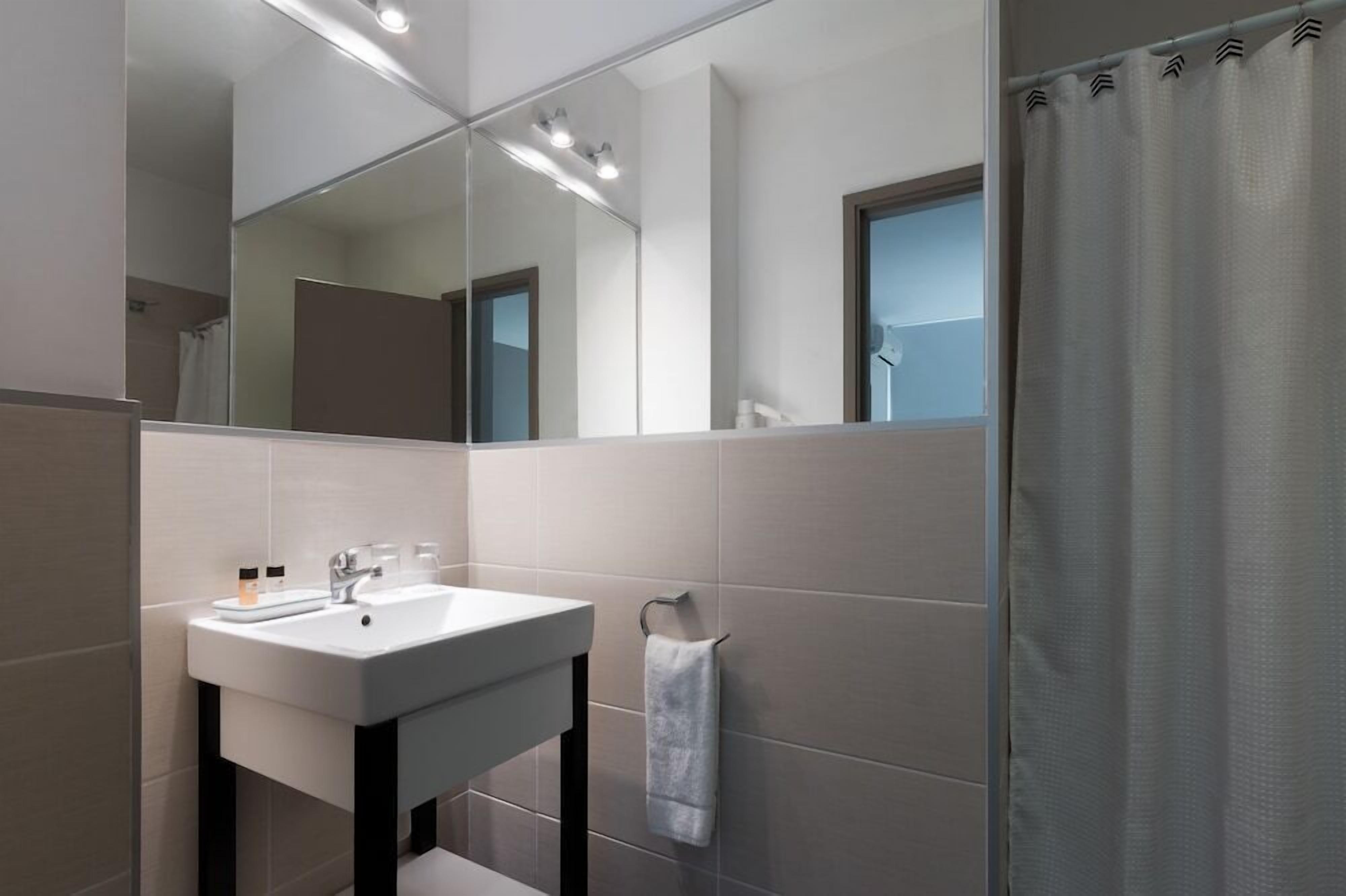 Un baño moderno con lavamanos, espejo y cortina de ducha blancos.