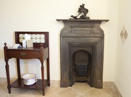 Una habitación con un escritorio de madera, una mesita con un cuenco y una chimenea con una escultura decorativa encima.