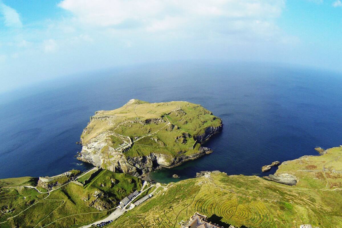An aerial view of a coastal area with a prominent rocky island, a small cove, and a road leading to a building.