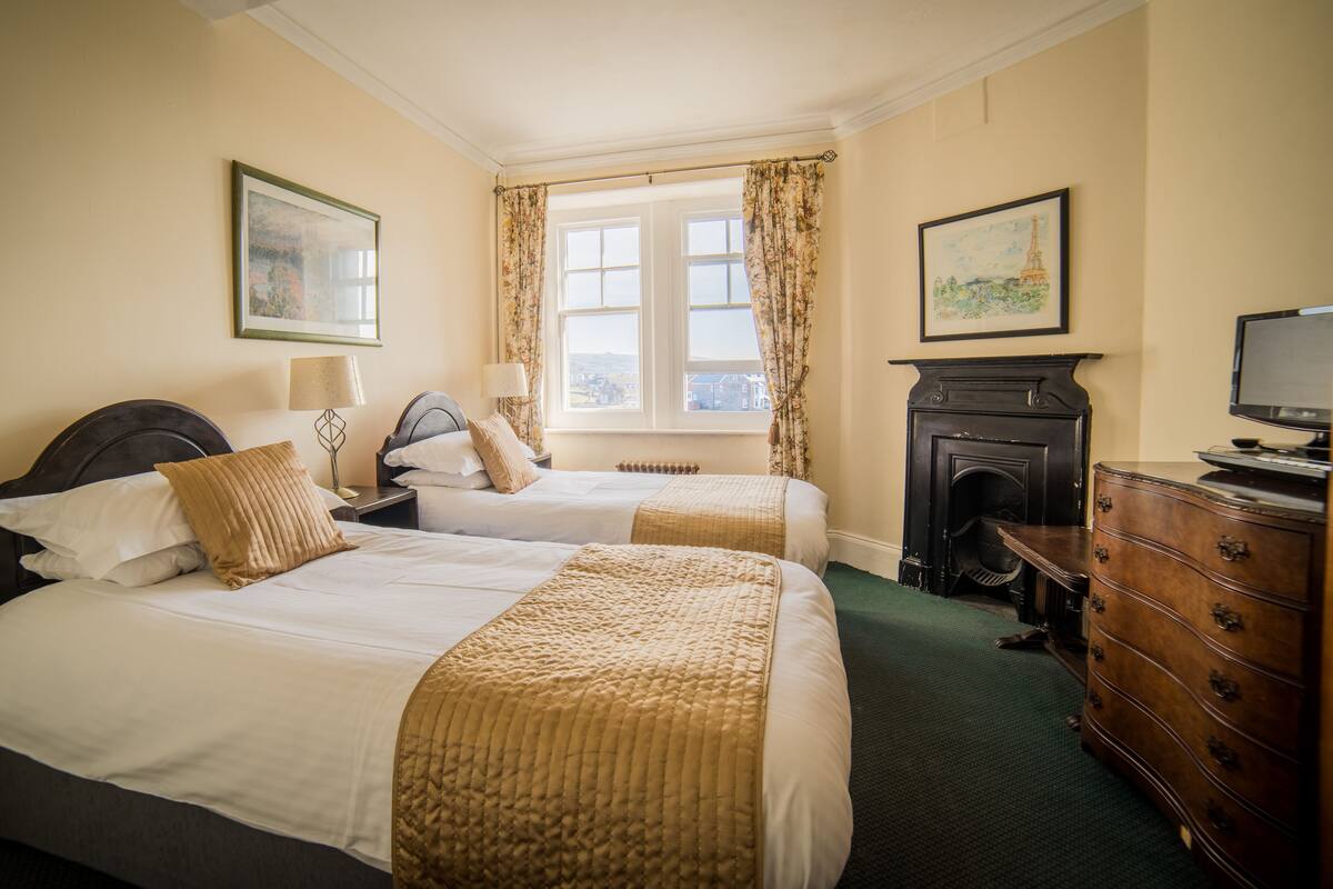 A hotel room with two beds, a fireplace, a television, and a window with curtains.