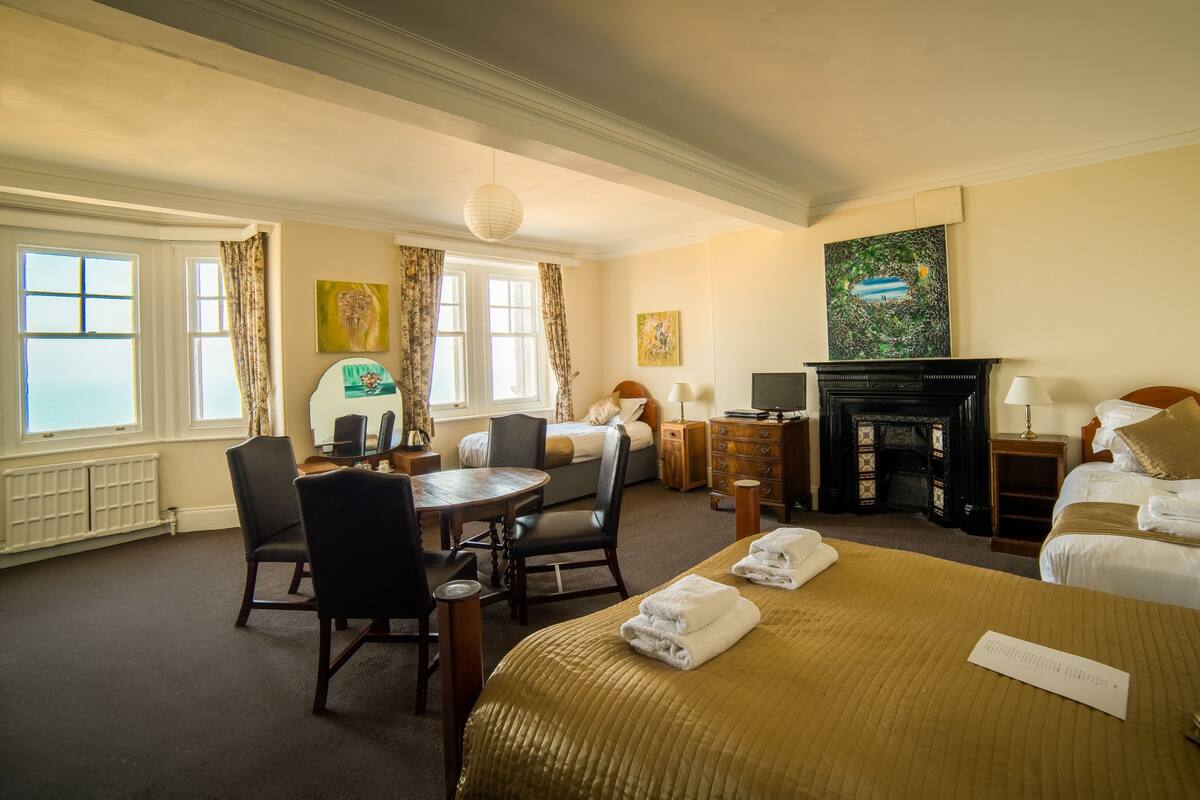 A hotel room with a bed, a desk, a chair, a fireplace, and artwork on the walls.