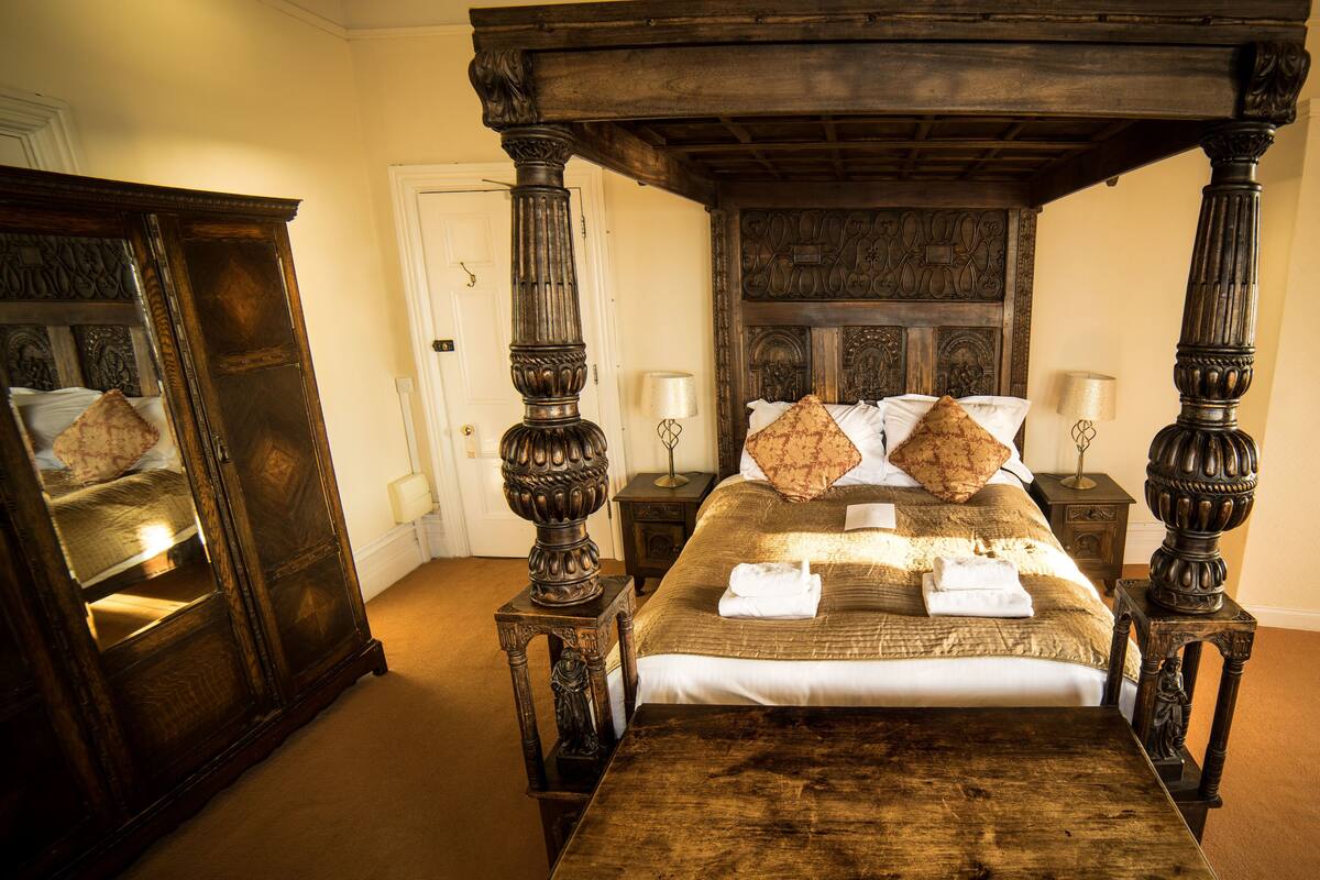 A four-poster bed with a wooden headboard, two nightstands, and a mirror on the left.