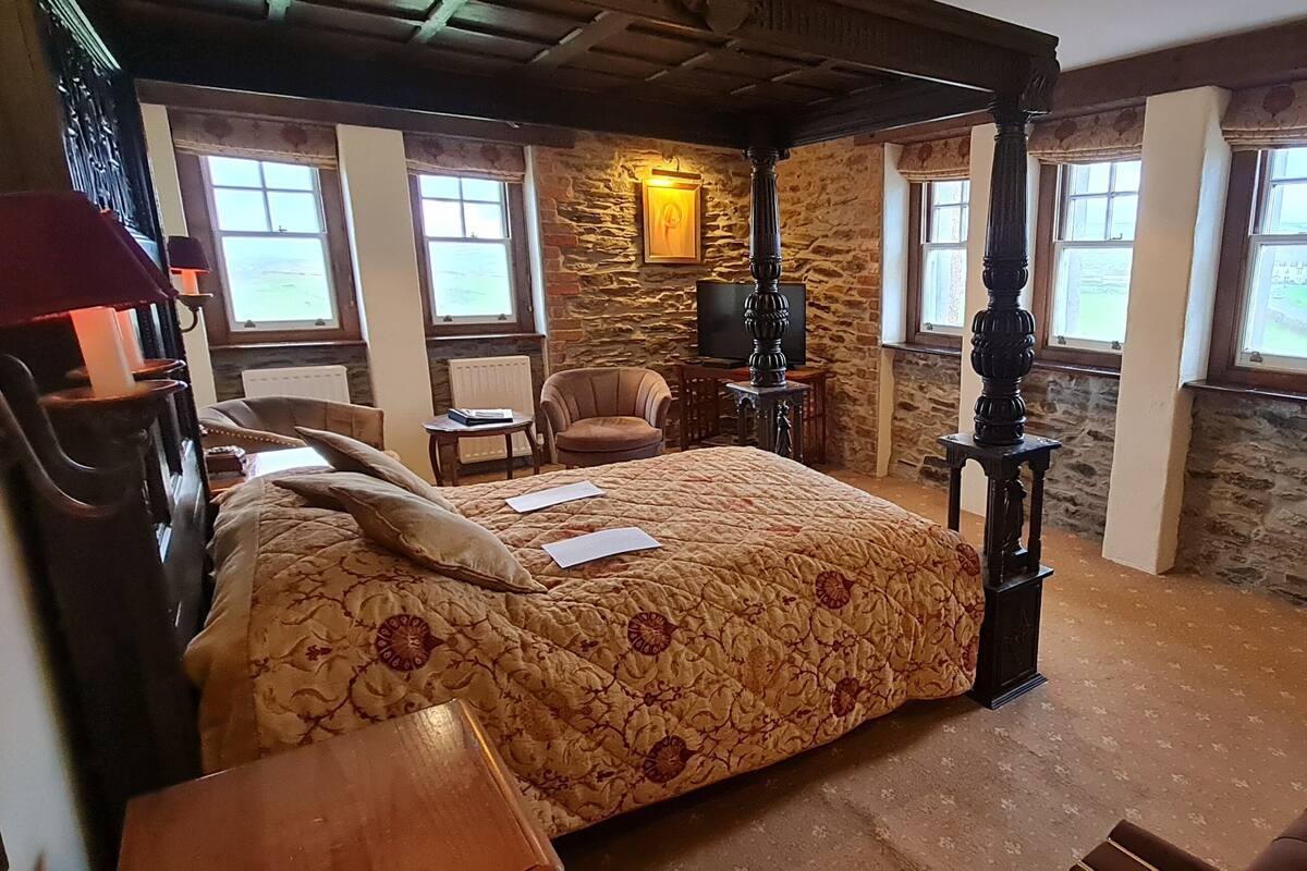 A traditional room with a four-poster bed, stone walls, a fireplace, and large windows.