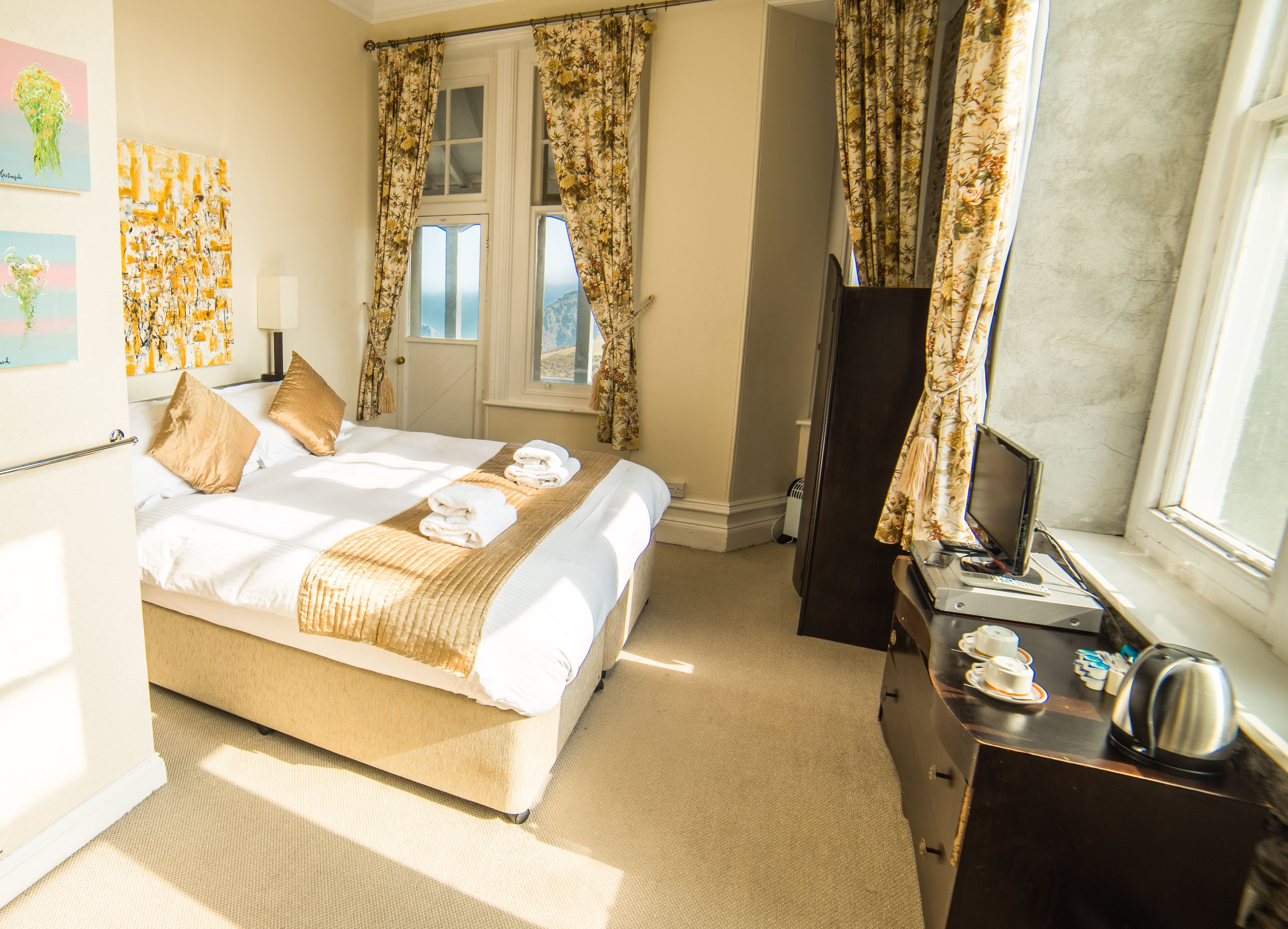 Une chambre d’hôtel avec un grand lit, un bureau avec un ordinateur, un miroir et une fenêtre avec des rideaux.