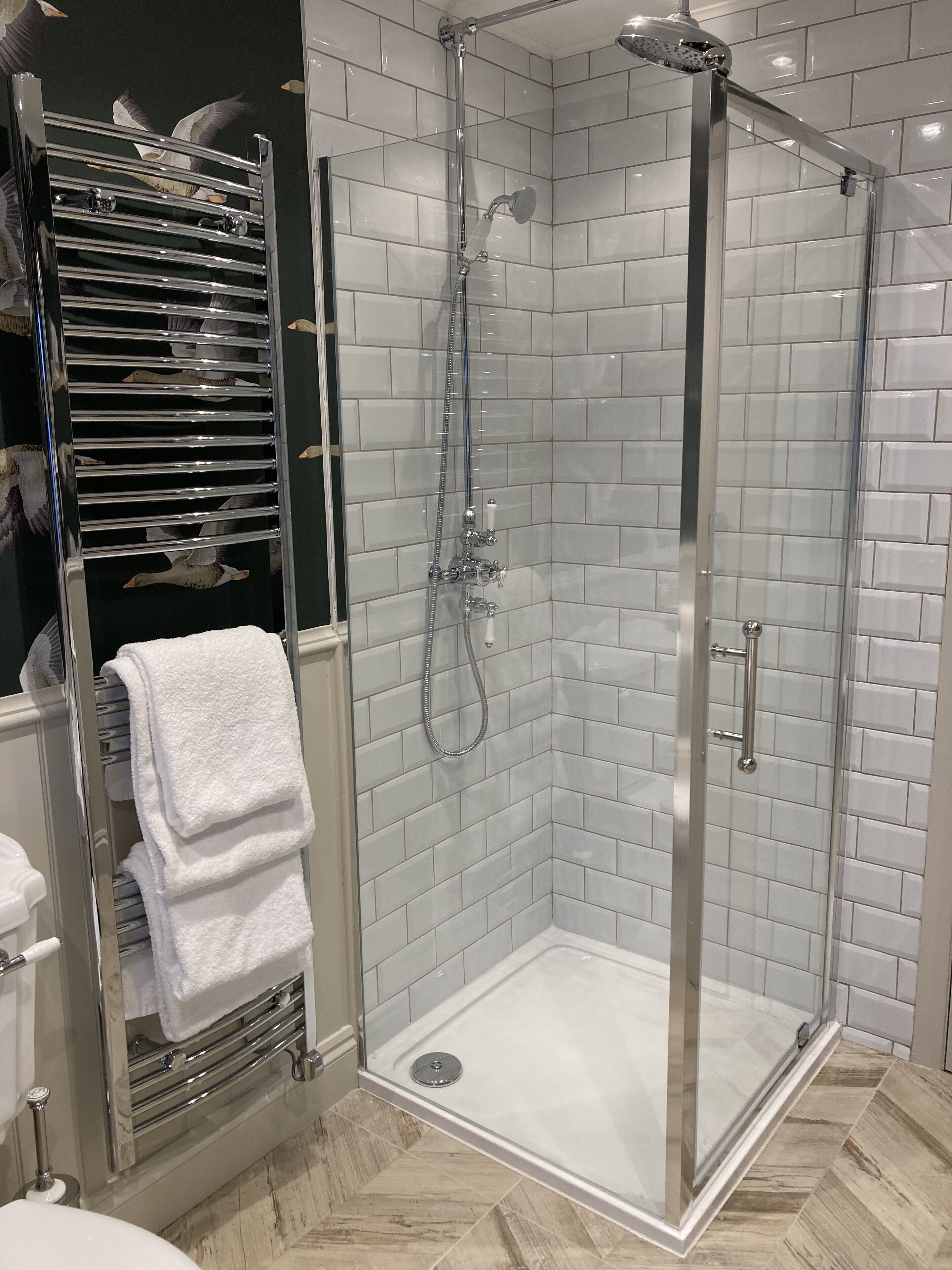 A modern bathroom with a glass-enclosed shower, white tiled walls, and a towel rack with folded towels.