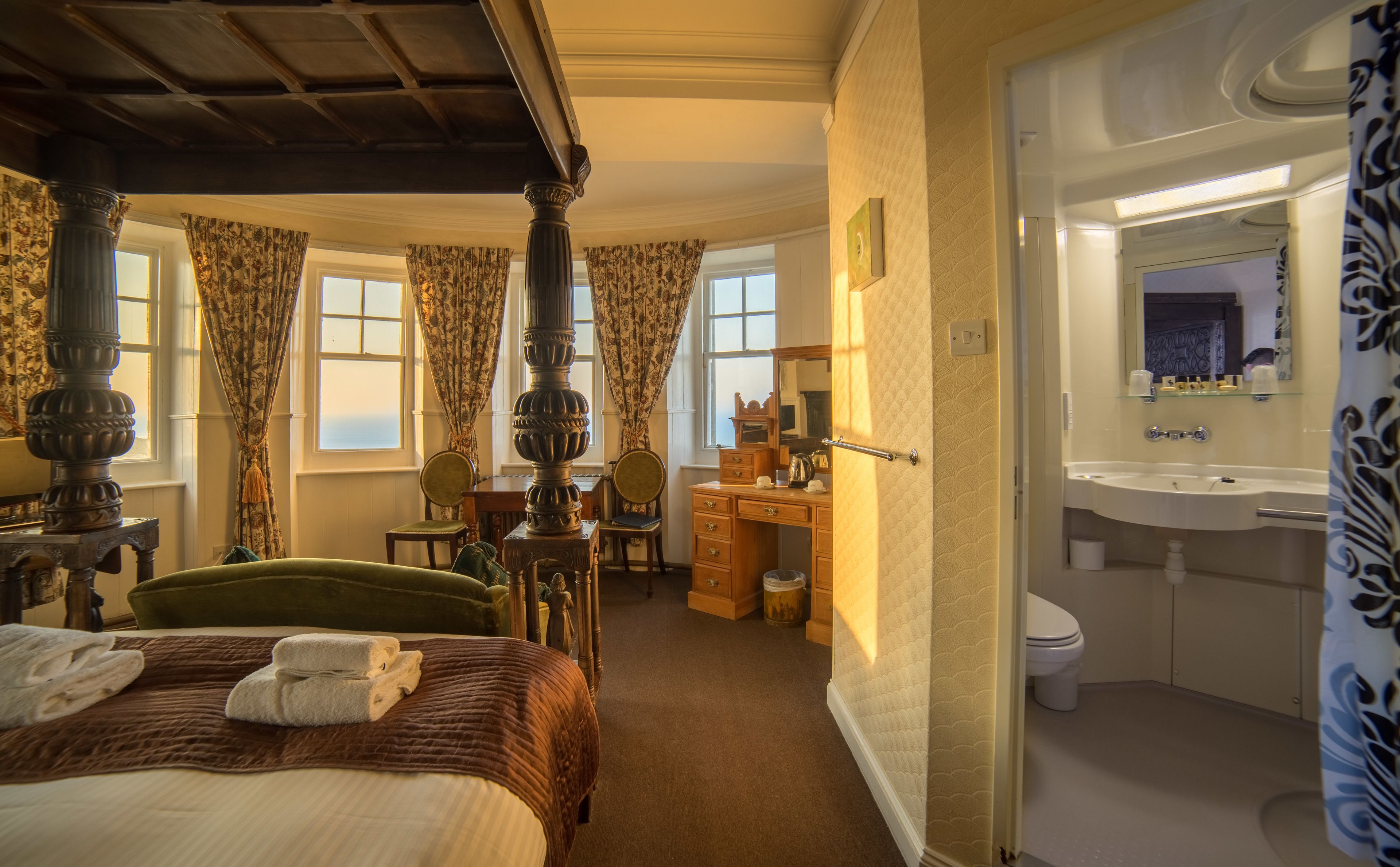 Un lit à baldaquin, un bureau avec une chaise, une salle de bain avec un lavabo et un miroir, et une vue sur la mer.