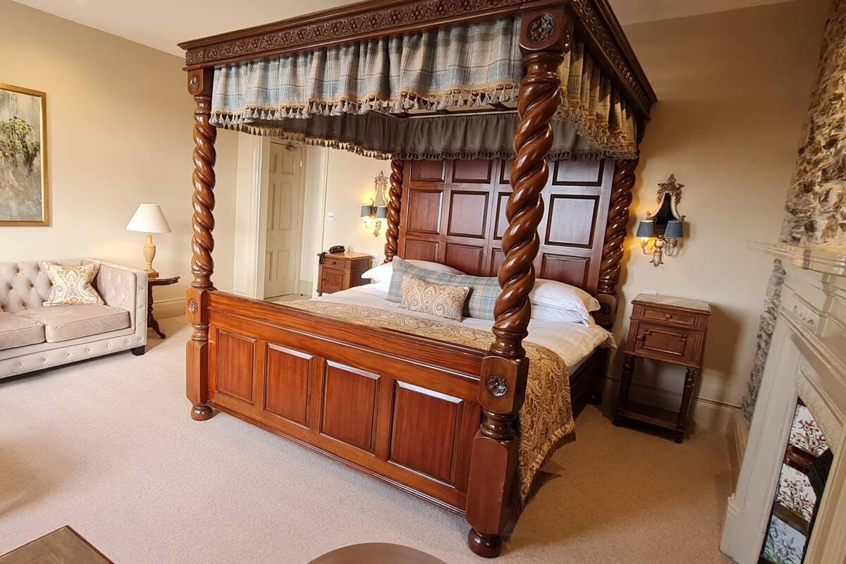 A bedroom with a four-poster bed, a sofa, a nightstand, a lamp, and a painting on the wall.