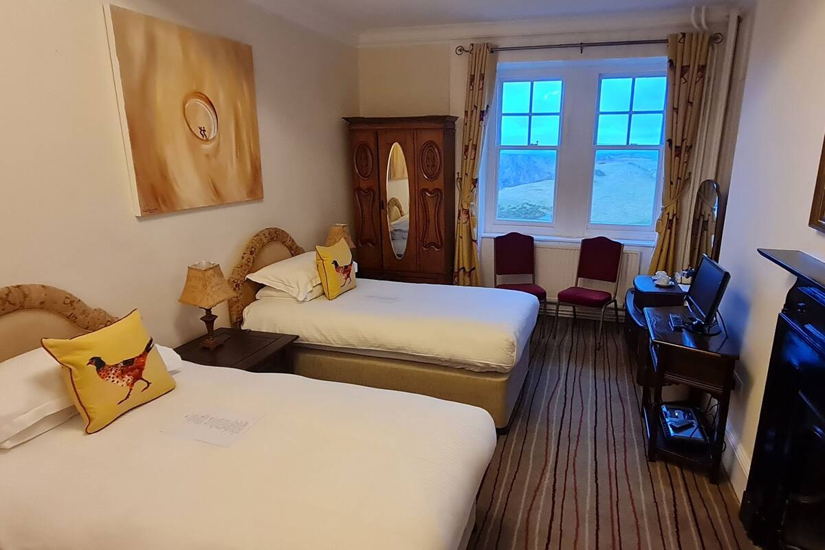 A hotel room with two beds, a desk, a chair, a wardrobe, and a large window.