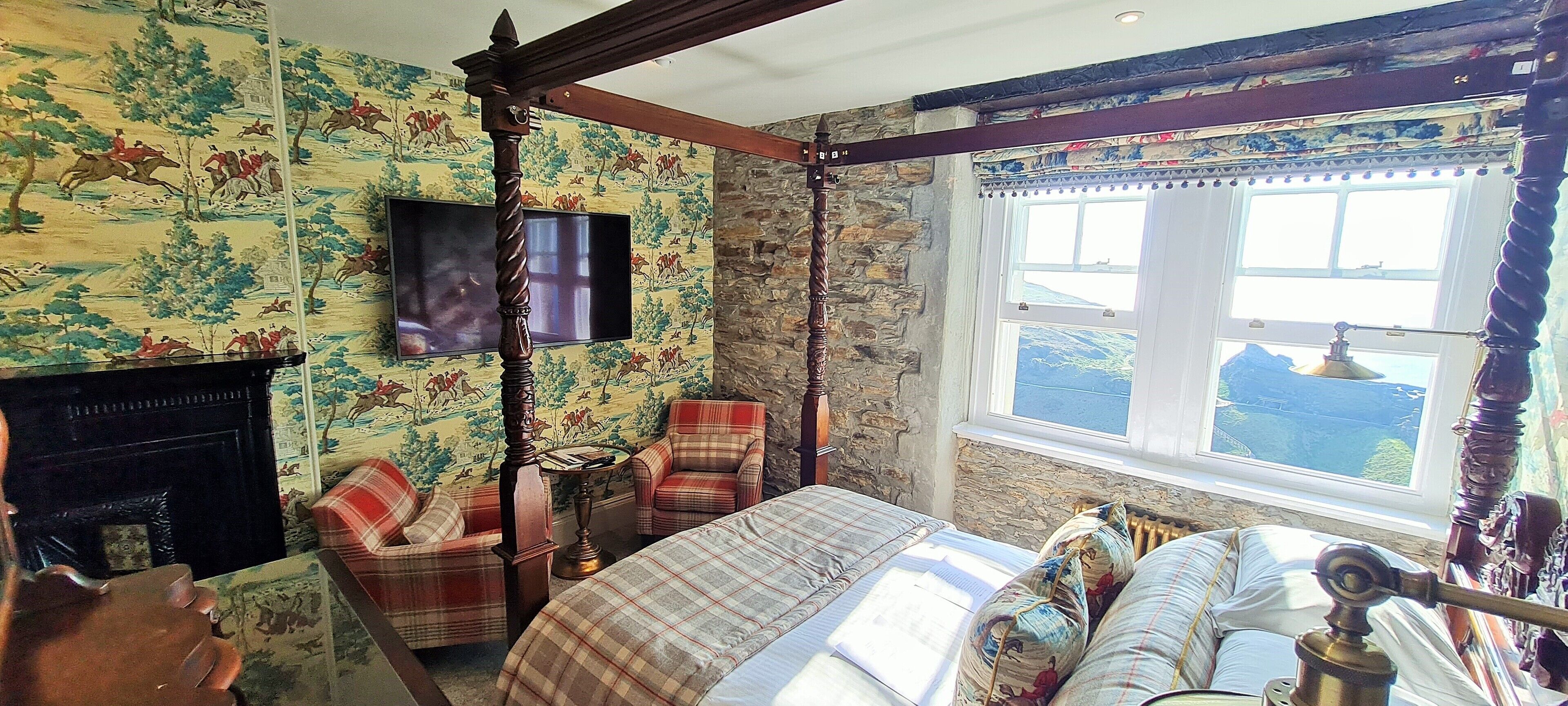 A traditional room with a bed, two chairs, a fireplace, a television, and a window with a view.