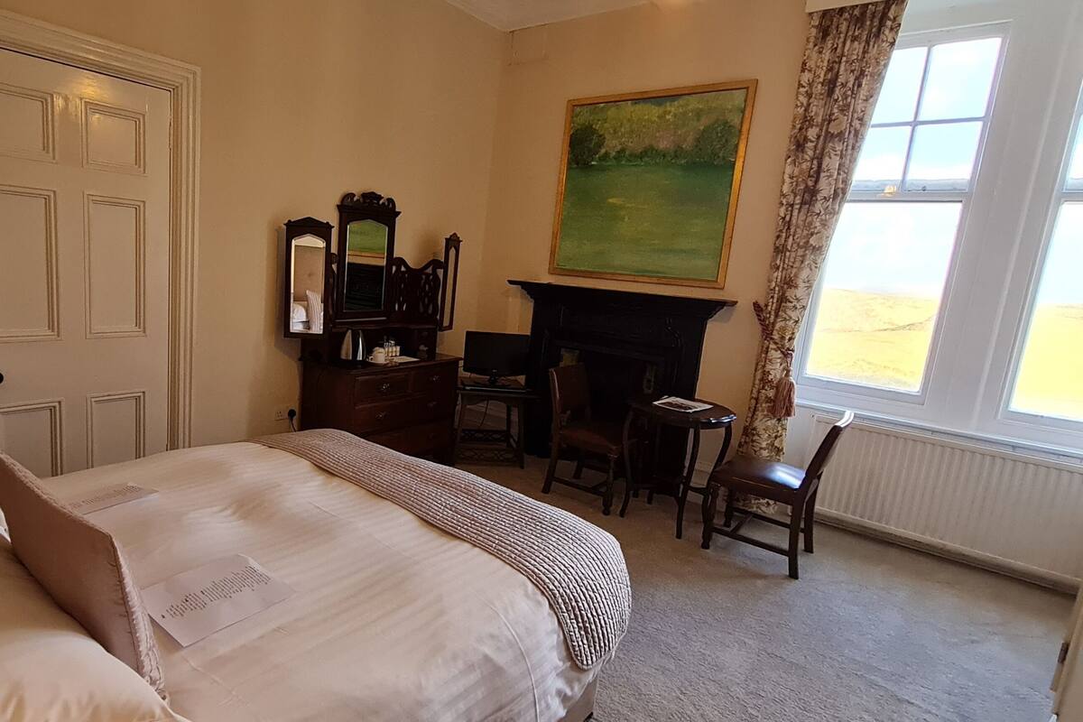 A hotel room with a bed, a desk, a chair, a fireplace, and a painting on the wall.