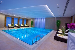 Una piscina interior moderna con sillones de descanso y suelo de baldosas.