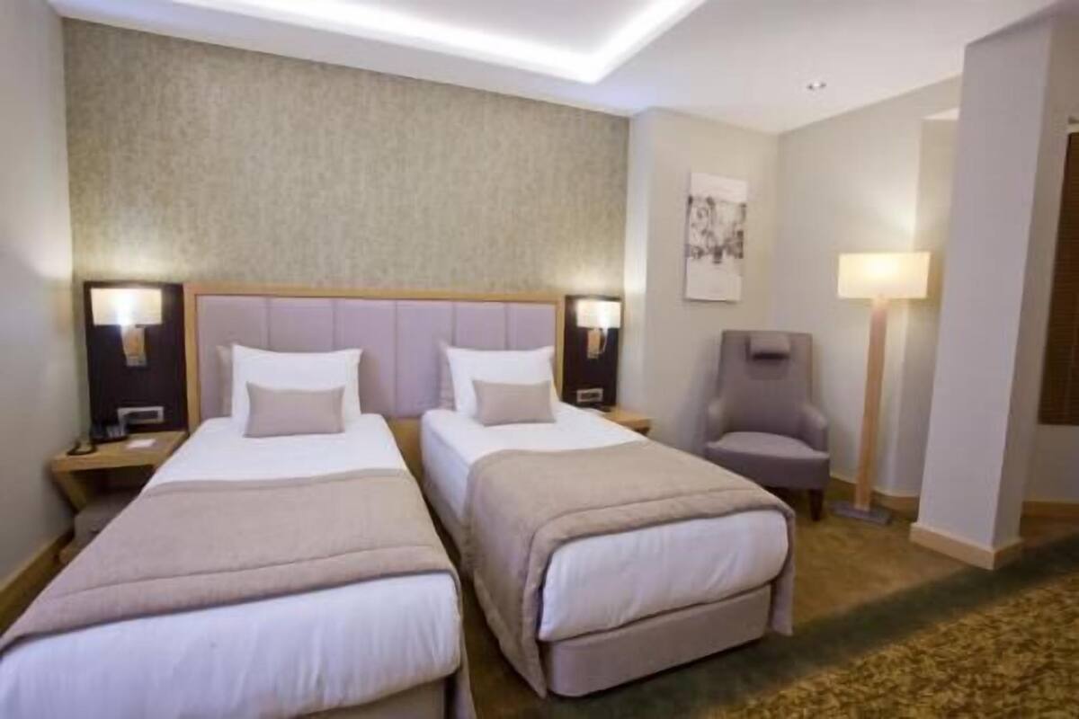 A hotel room with two beds, a chair, a desk, and a lamp.